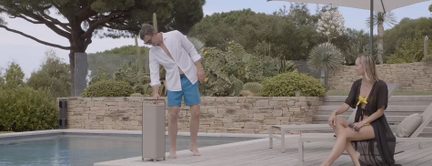 Bærbar udendørs højttaler i beige søjleformat ved kanten af en pool med håndtag på toppen