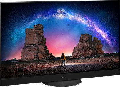 Panasonic TX-55MZ2000E-fladskærm, der viser et billede af en mand, der står foran enorme klippeformationer under en livlig, stjerneklar himmel