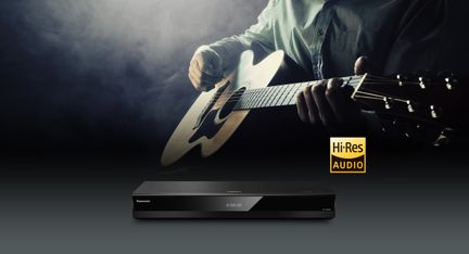 Leitor de áudio preto em metal escovado e plástico brilhante, vista frontal, fachada lisa com tela digital central exibindo 0:00.00 e logotipo branco à esquerda