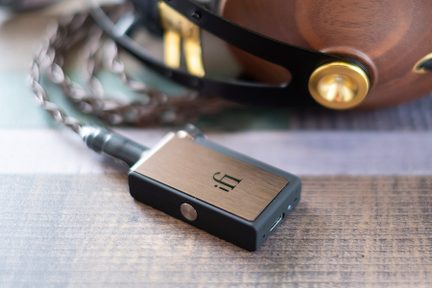 Kompakt rektangulær sort og børstet metal audioforstærker med cirkulær knap, stik og USB-port, snoet kabel, træhovedtelefoner