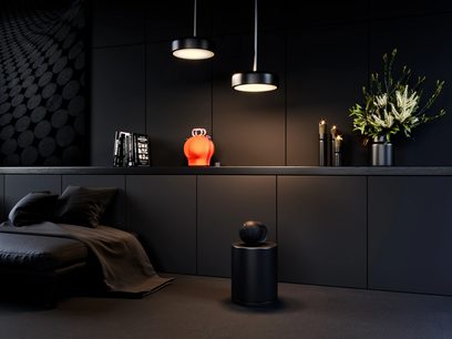 DEVIALET PHANTOM II 98 DB wireless connected speaker, matte black, vivid orange, cylindrical shape, placed on a black cabinet, dark interior setting