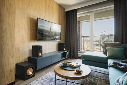 Sala moderna com sofá turquesa, mesa de centro redonda de madeira, móvel de TV azul, alto-falantes pretos, grande janela