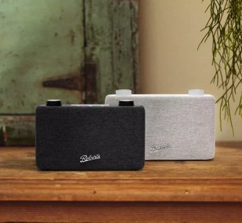 To rektangulære Roberts Bluetooth-høyttalere i svart og lysegrått stoff på et tremøbel, i en vintage-inspirert interiørstil