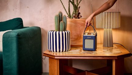 Holztisch, blau-weiß gestreifter Keramiktopf mit Kaktus, gestreifte Lampe, blaues Radio mit Antenne, gehalten von einer Hand