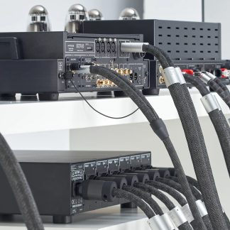 Rückansicht von schwarzen Audiogeräten mit goldenen Anschlüssen, schwarzen ummantelten Kabeln und silbernen Metallzylindern auf weißen Regalen