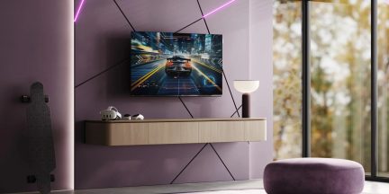 An der Wand montierter Flachbildfernseher über einem hängenden Möbelstück, angezeigtes Autorennspiel in einem modernen violetten Wohnzimmer