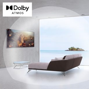 Dolby Atmos-fladskærm på metalstativ i hvidt rum, skærmen viser tropisk ø og kvinde med langt hår