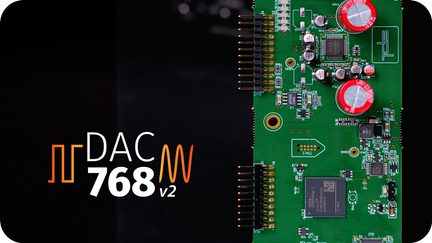 Zielona płytka elektroniczna z widocznymi komponentami, dwa czerwone kondensatory, złote złącza, tekst "DAC 768 v2" po lewej stronie