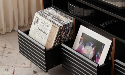 Svart møbel med åpne, riflede skuffer som inneholder vinylplater og omslag, toppflate med elektroniske gjenstander