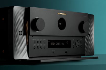 Melns Marantz mājas kinozāles pastiprinātājs ar teksturētu alumīnija priekšpusi, diviem lieliem kloķiem un ekrānu ar uzrakstu MAIN ZONE On