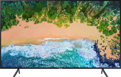 Samsung UE49NU7105-fladskærm, der viser en sandstrand og brusende bølger under en frodig, tropisk skov