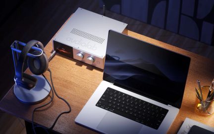 Rektangulär ljudförstärkare i silverfärgad aluminium, frontpanel med liten orange skärm och två räfflade rattar, sedd snett uppifrån på ett ljust träskrivbord