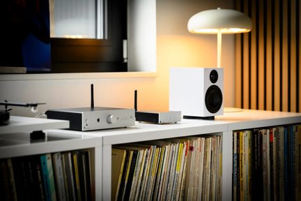Srebrny zestaw hi-fi z dwiema antenami, małym białym głośnikiem i gramofonem na szafce na płyty winylowe