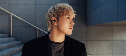 Person set i profil med sort trådløs in-ear-øreprop i plastik, baggrund med trapper og betonvægge