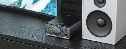 Rectangular black metal audio case, three-quarter front left view, featuring a large silver knob with blue backlighting, five aligned LEDs, and two jack sockets on the front panel