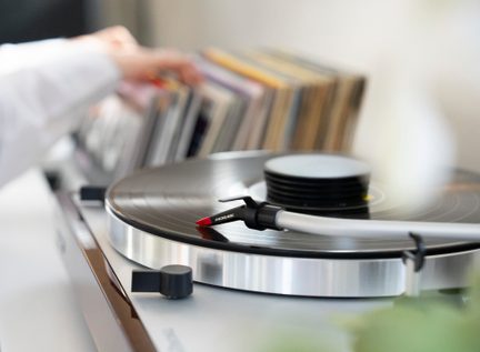 Gramofon s tonskim krožnikom in črnim diskom, roka na ozadju prilagaja diske