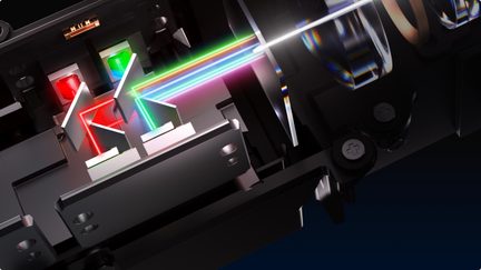 Schrägschnittansicht eines schwarzen optischen Moduls aus Metall und Glas mit Prismen und Spiegeln sowie roten, grünen und blauen Strahlen