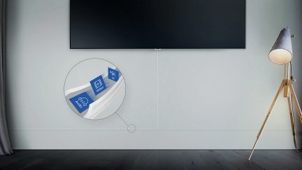 TV-skærm, der viser en skyikon, designlampe med trebensstativ i lyst træ og metal i et rum med hvide vægge