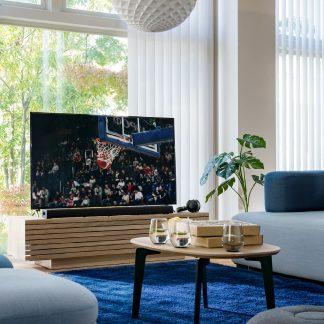 TV som visar en basketmatch i ett modernt vardagsrum, grå soffa, soffbord i trä, grön växt