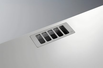 Obdélníková kovová mřížka s pěti štěrbinami, zapuštěná do matně bílého panelu, pohled shora