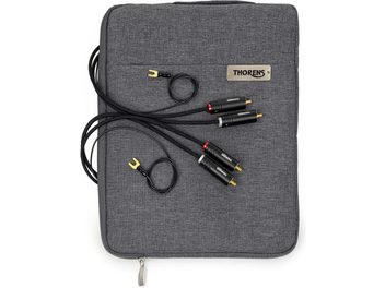 Czarny kabel phono Thorens PhonoConnect PHS 150 RCA-RCA o długości 1,5 m z oplotem tekstylnym, czarne wtyki RCA z oznaczeniami czerwonym i białym, pozłacane końcówki oraz żółte widełki uziemiające, widok z góry nałożony na szarą materiałową saszetkę