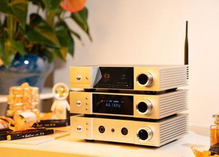 Stack of three gold aluminum hi-fi audio modules, three-quarter front right view, front panels with black displays, large circular knobs, metal buttons, headphone jacks, and rear black antenna