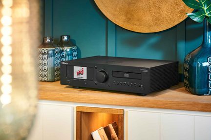 Mat sort metal hi-fi kabinet set fra højre forfra i trekvart vinkel, med farvedisplay, stor central drejeknap og CD-skuffe på fronten