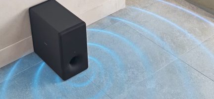 Rechteckiger schwarzer Subwoofer, aus der Vogelperspektive betrachtet, an einer Wand positioniert, grauer gefliester Boden, sichtbare blaue Wellen