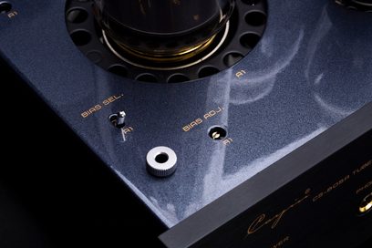 Primer plano en vista superior ligeramente oblicua del chasis metálico negro metalizado del Cayin CS-805A, mostrando la base circular perforada de una lámpara, una palanca cromada «BIAS SEL.», un tornillo de ajuste «BIAS ADJ.», un botón moleteado plateado y la serigrafía dorada de la marca.