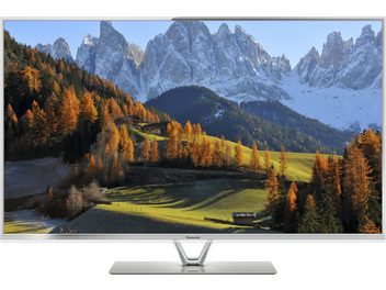 Sněhem pokryté horské panorama s jehličnatými lesy v podzimních barvách a travnatým údolím pod jasně modrou oblohou