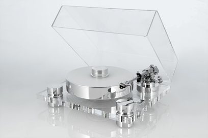 Transrotor Bellini RB330 hi-fi pladespiller set fra venstre forfra i trekvart vinkel, med base og hævet låg i transparent akryl, massivt cirkulært pladetallerken og cylindriske støtter i sølvpoleret aluminium, tonearm til højre