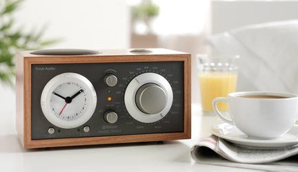 Træradio med lys træfarve, grå front, analog ur til venstre, stor knap til højre, 3/4 forfra set