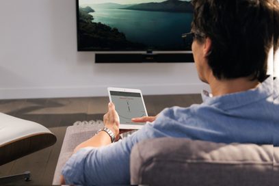 Mand set bagfra, der holder en tablet med et diagram foran et stort tv-skærm, der viser et maritimt landskab