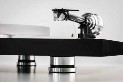 Gira-discos hi-fi preto em close-up, mostrando o braço de leitura e a célula Pick it Pro, com pés cilíndricos de alumínio