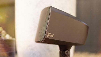 Brown plastic speaker with metal grille, Klipsch logo, mounted on a swivel stand, three-quarter view