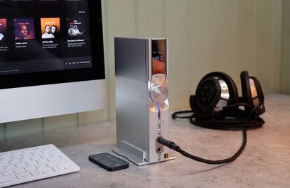 Audio konvertor DAC iFi Audio IDSD NEO Performance Edition ve stříbrné barvě, přední pohled, umístěný vertikálně na dřevěném stole