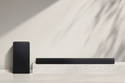 Rektangulär svart soundbar med metallgaller och svart subwoofer i plast, sedd framifrån, placerade på en vit, fläckig yta