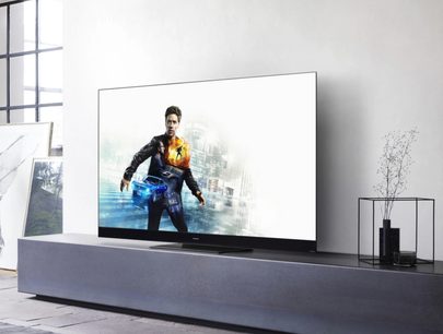 Panasonic TX-65HZ2000E-fladskærm, der viser et billede af en mand i jakkesæt, der holder et futuristisk våben foran et sløret bybaggrund