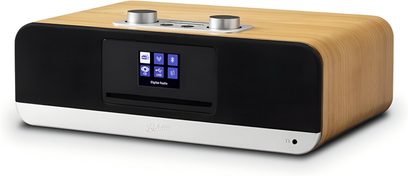 Roberts BluTune 300 bordradio set fra tre kvart forfra, rektangulært lys trækabinet med afrundede hjørner, sort front med en central farveskærm og en vandret sprække, nederste sølvfarvede bånd med et minijack-stik og to store aluminiumsdrejeknapper på det øverste panel