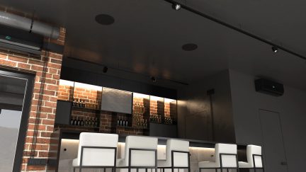 Innenansicht einer Bar mit Metalltheke, weißen Hockern, Ziegelwand, Regalen mit Flaschen, dunkler Decke und integrierter Beleuchtung