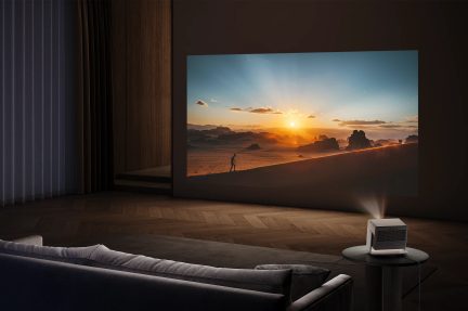 Salotto con divano grigio, tende scure, proiettore su tavolo rotondo, immagine di tramonto proiettata sul muro