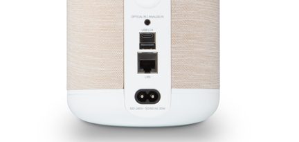 Galinė beige audinio ir balto plastiko kolonėlės pusė, optinė/analoginė 3,5 mm jungtis, USB‑C, USB‑A, LAN ir C7 maitinimas