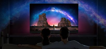Panasonic TX-48JZ980E-fladskærm, der viser et billede af geologiske klipper oplyst af en farverig galakse, set bagfra med to personer siddende foran