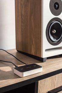 Hvid Octavio Stream netværksaudioafspiller, tæt forfra, placeret på et lyst trægittermøbel, tilsluttet højttalere