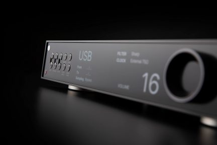 Juodo garso įrenginio vaizdas iš kampo su apvaliais mygtukais, skaitmeniniu ekranu „USB“ ir „16“, garsumo reguliatoriumi dešinėje