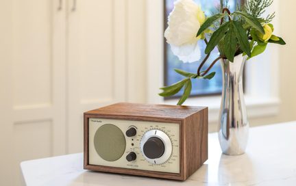 Radio in legno marrone, frontale color crema con griglia metallica e grande pulsante di regolazione, vista a tre quarti