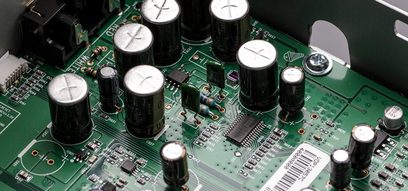 Grønt printplade med flere sølvfarvede elektrolytiske kondensatorer og modstande monteret på det, tæt på visning