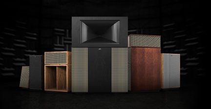 Skupina hi-fi reproduktorů z dřeva a látky, provedení ořech a černá, velký centrální pavilon, pohled zepředu na tmavém pozadí
