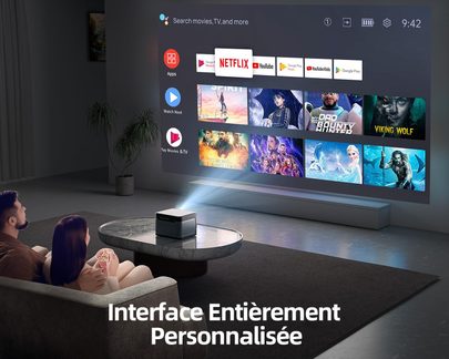 Televisor que muestra la interfaz de Netflix con miniaturas de películas y series, pareja sentada en un sofá en una sala de estar oscura