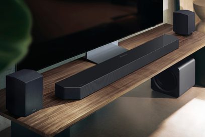 Samsung Soundbar HW‑Q995F in schwarzem, gitterbespannten Metall, aus der Dreiviertel-Perspektive von oben gesehen, langes rechteckiges Gehäuse mit abgeschrägten Ecken, dazu passende würfelförmige Satellitenlautsprecher und ein Subwoofer